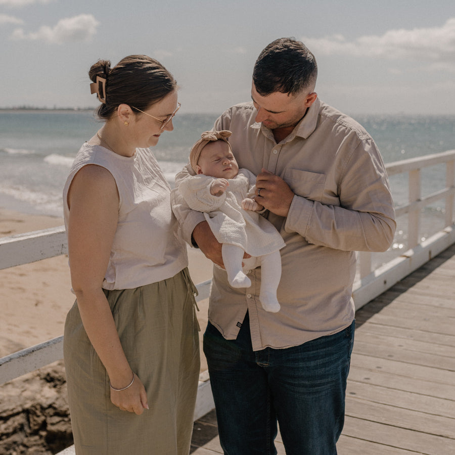 Family of three standing on a wooden pier by the ocean